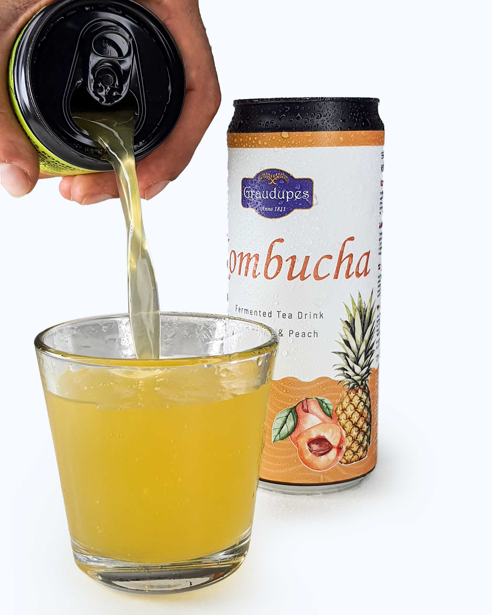 hand pouring a fizzy drink into a glass from a 330ml can, Graudupes Pineapple & Peach Kombucha - Natural Fermented Tea Drink With Fruit Juice and Probiotics.