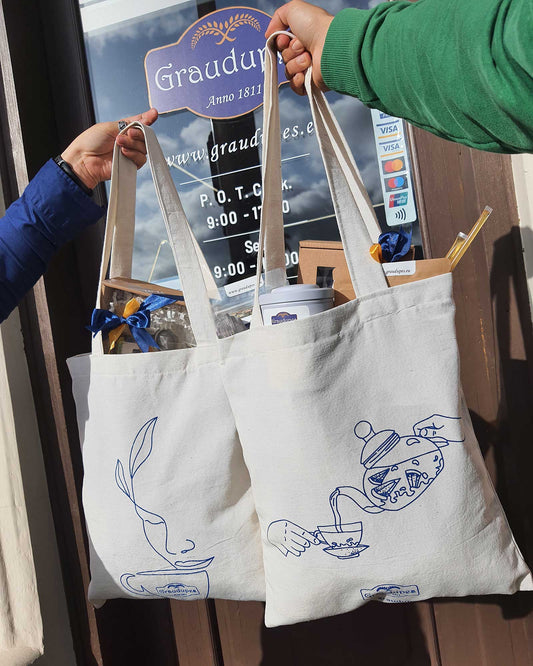 Natural Cotton Tote Bag [40cm X 35cm] man and woman hands holding 2 Eco-friendly Canvas Shopping Bags full of items and gifts from Graudupes shop in front of Graudupes shop in Saldus, Latvia.