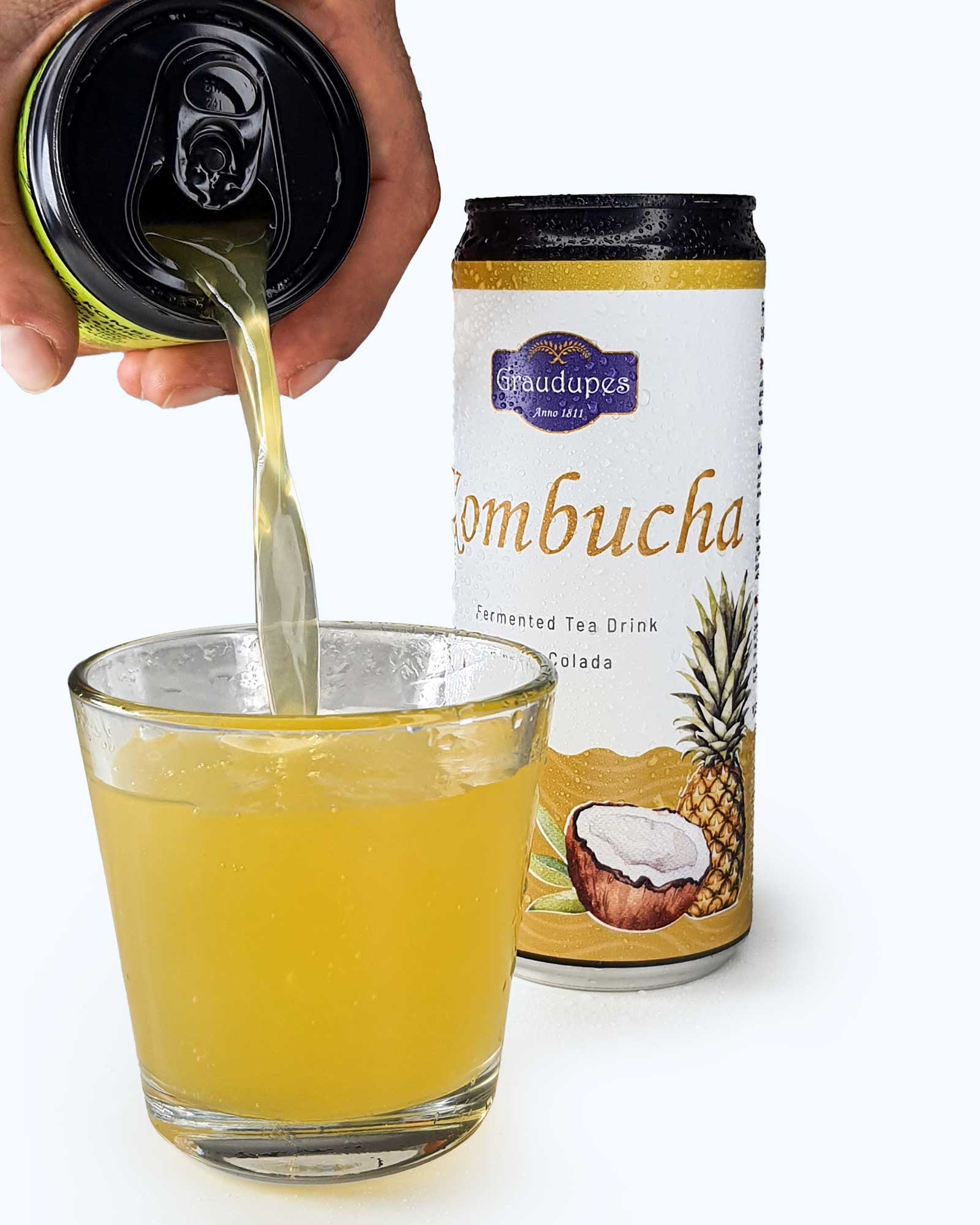 hand pouring a fizzy drink from a 330ml can into a glass, Graudupes Coconut & Pineapple Kombucha (Piña Colada) - Natural Fermented Tea Drink With Fruit Juice and Probiotics.